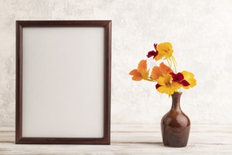 Wooden frame with orange nasturtium flowers in ceramic vase on gray concrete background. side view,