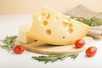 Various types of cheese with rosemary and tomatoes on wooden board on a white wooden background and