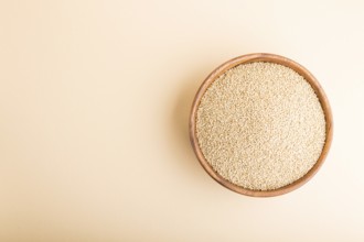 Wooden bowl with raw white quinoa seeds on a pastel orange background. Top view, flat lay, copy