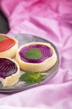 Sweet tartlets with jelly and milk cream with cup of coffee on a black concrete background and pink