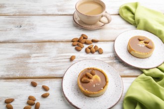 Sweet tartlets with almonds and caramel cream with cup of coffee on a white wooden background and