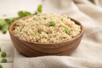 Quinoa porridge with green pea in wooden bowl on a white wooden background and linen textile. Side