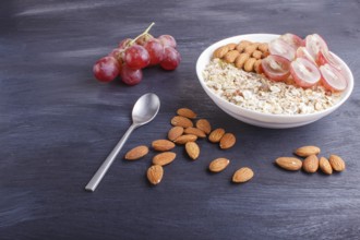 A plate with muesli, almonds, pink grapes on a black wooden background. close up. copy space