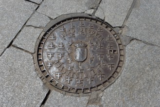 Manhole cover with the coat of arms and inscription of Segovia on a cobbled street, manhole cover,