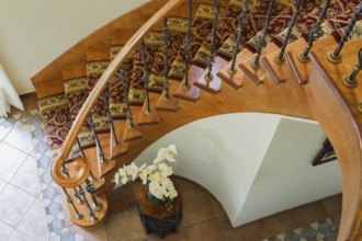 Top view of wooden spiraling staircase with burgundy and cream coloured rug runner and brass rods