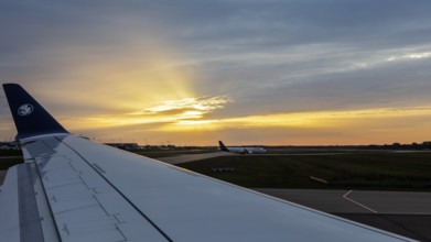 View from aeroplane on runway, wings and bright sunset in the background, flight, aerial