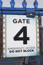 Close-up of posted emergency access gate 4 Do Not Block notice sign on blue painted steel and wire