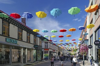 Pedestrian zone with colourful umbrellas stretched across the street, shops and people, Nidarelva,