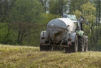 Slurry is spread on a field with a tractor from a slurry tanker to fertilise the farmland, North