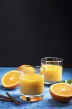 Glass of orange juice on a black and blue background. Hard light, contrast. Side view, copy space