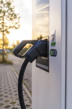 Close-up of an electric charging plug connected to a charging station at sunset, Calw, Black