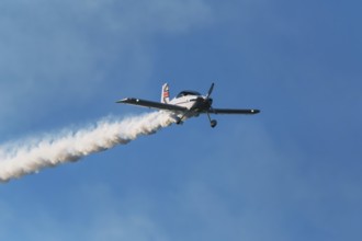 Stunt aerobatic plane performing stunts in blue sky with smoke trail. Concept of speed, difficulty,