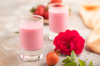 Sweet strawberry liqueur in glass on a gray concrete background and orange textile. side view,