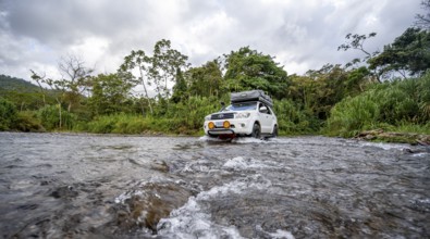 Toyota off-road vehicle with roof tent drives through a wide river in the rainforest, Alajuela