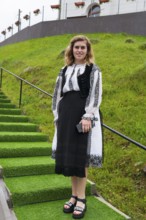 Young woman in traditional dress standing on a green staircase, woman in traditional traditional