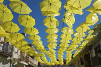 Artistic installation of yellow umbrellas over a street, enveloped by balconies and old buildings