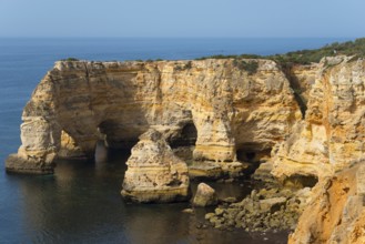 Steep cliffs and craggy rocks jut out of the calm sea on a clear day, Praia da Marinha, Lagoa,