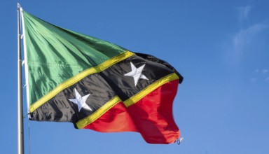 The flag of St Kitts, Caribbean, fluttering in the wind, isolated against a blue sky