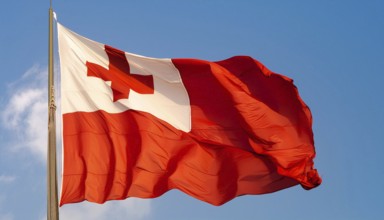 The flag of Tonga, Pacific island state, flutters in the wind, isolated against a blue sky