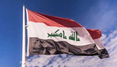 The flag of Iraq flutters in the wind, isolated against a blue sky