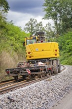 Yellow construction machine on railway tracks in wooded surroundings, track construction, Hermann