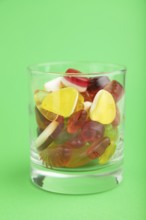 Various fruit jelly candies in drinking glass on green pastel background. side view, close up