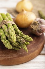 Bunch of fresh green asparagus, garlic, onion on white wooden background. Side view, selective