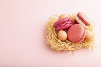 Purple and pink macaroons and chocolate eggs in decorative paper nest on pink pastel background.