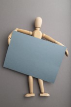 Wooden mannequin holding blue blank poster on gray pastel background. copy space, isolated,