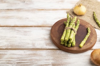 Bunch of fresh green asparagus, garlic, onion on white wooden background. Side view, copy space.