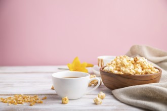 Popcorn with caramel in wooden bowl and a cup of coffee on a white and pink background and linen