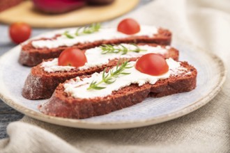 Red beet bread sandwiches with cream cheese and tomatoes on gray wooden background and linen