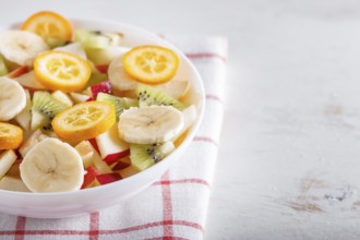 Vegetarian salad of bananas, apples, pears, kumquats and kiwi on linen tablecloth, close up,