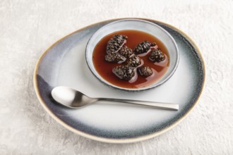 Pine cone jam on ceramic plate on gray concrete background. Side view, close up