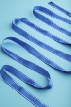 Blue ribbon on a blue pastel background. Celebration concept. Side view, close up