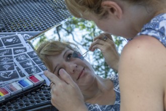 Detroit, Michigan, A woman uses a mirror to paint a design on her face at the annual 'Summer