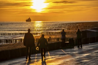 Sunset on the beach of Zoutelande, beach with wooden pile breakwaters, tourists, cargo ship sailing