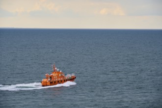 An orange pilot boat sailing on the open sea under a cloudy sky, Kiel, Schleswig-Holstein, North