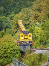 Yellow crane from Leonhard Weiss works on a railway line, surrounded by lush nature and trees,