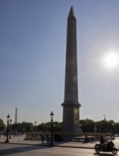 Sunbeams behind an obelisk, Eiffel Tower in the background, a motorbike passing by, Paris