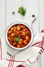 Potatoes stewed with meat, in tomato sauce, with spices and herbs, no people, on a white table