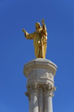 Golden statue of Jesus on a high column in front of a blue sky, Christ statue, Santuario de Fatima,