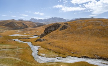 River Kol Suu winds through a mountain valley with hills of yellow grass, Naryn Province,