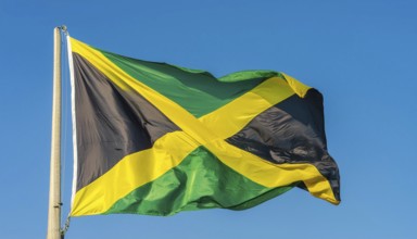 The flag of Jamaica flutters in the wind, isolated against a blue sky