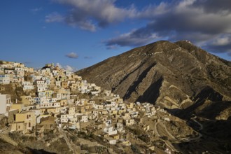 A rustic village stretches beneath a mountainous backdrop with dramatic clouds, Colourful mountain