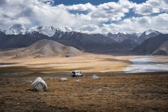 Off-road vehicle on a gravel track, glaciated and snow-covered peaks, Ak Shyrak Mountains, near