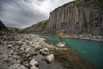 Tourist standing by the river in Stuðlagil Canyon, turquoise blue river between basalt columns,