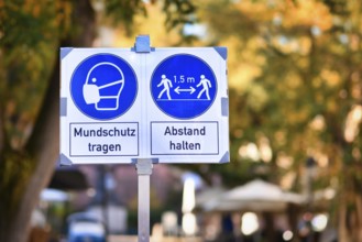 Signs for face mask and distance requirement in German city center with text saying wear face mask