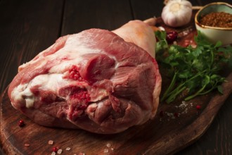 Raw pork knuckle, on a wooden chopping board, with spices, close-up, top view, no people