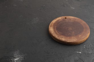 Empty round wooden cutting board on black concrete background. Side view, copy space